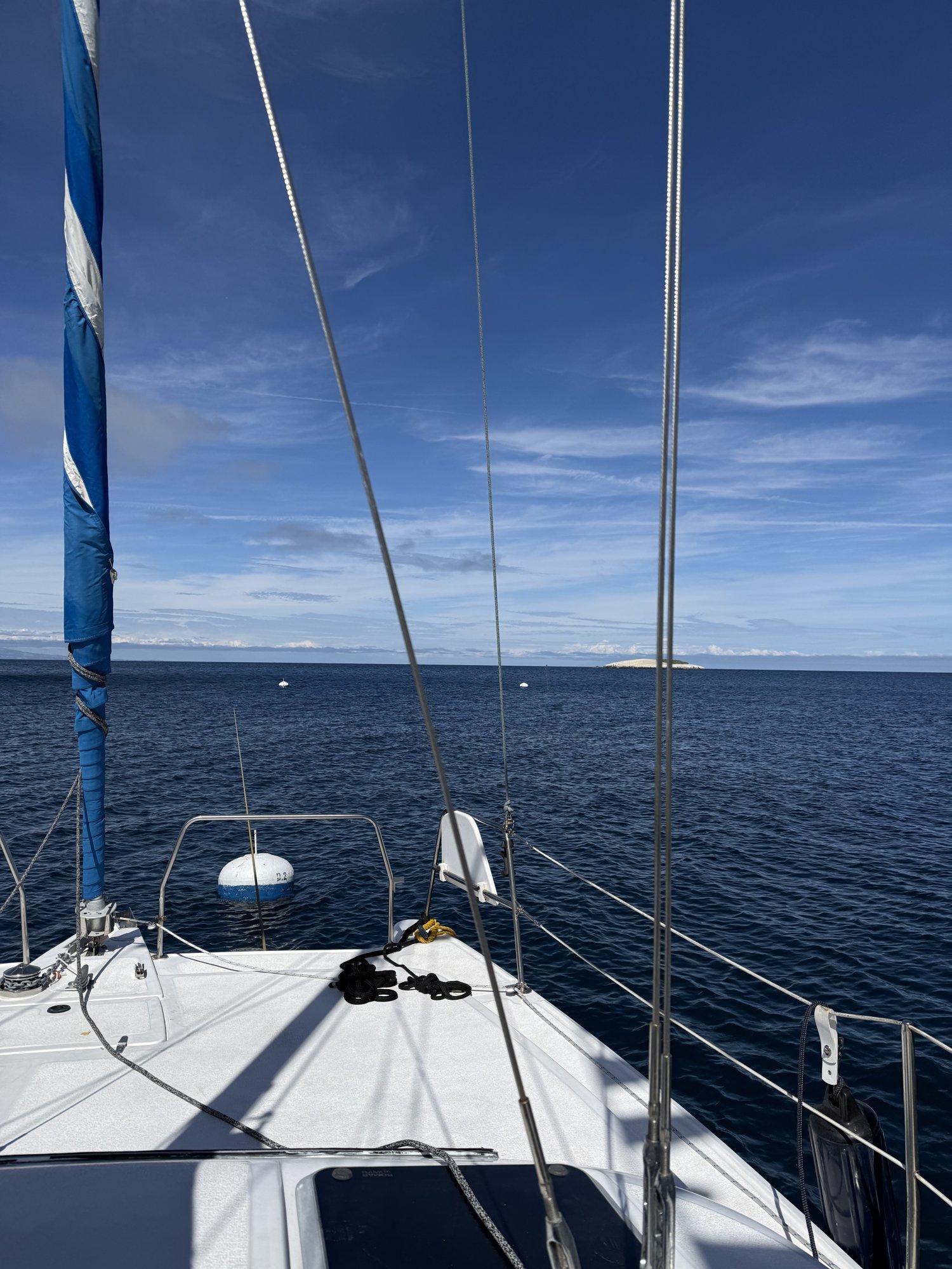 The view from the deck of a 37-foot catamaran moored at Two Harbors, looking past the furled jib and rigging across Harbor Reef toward Bird Rock in the distance on a clear, bright day.