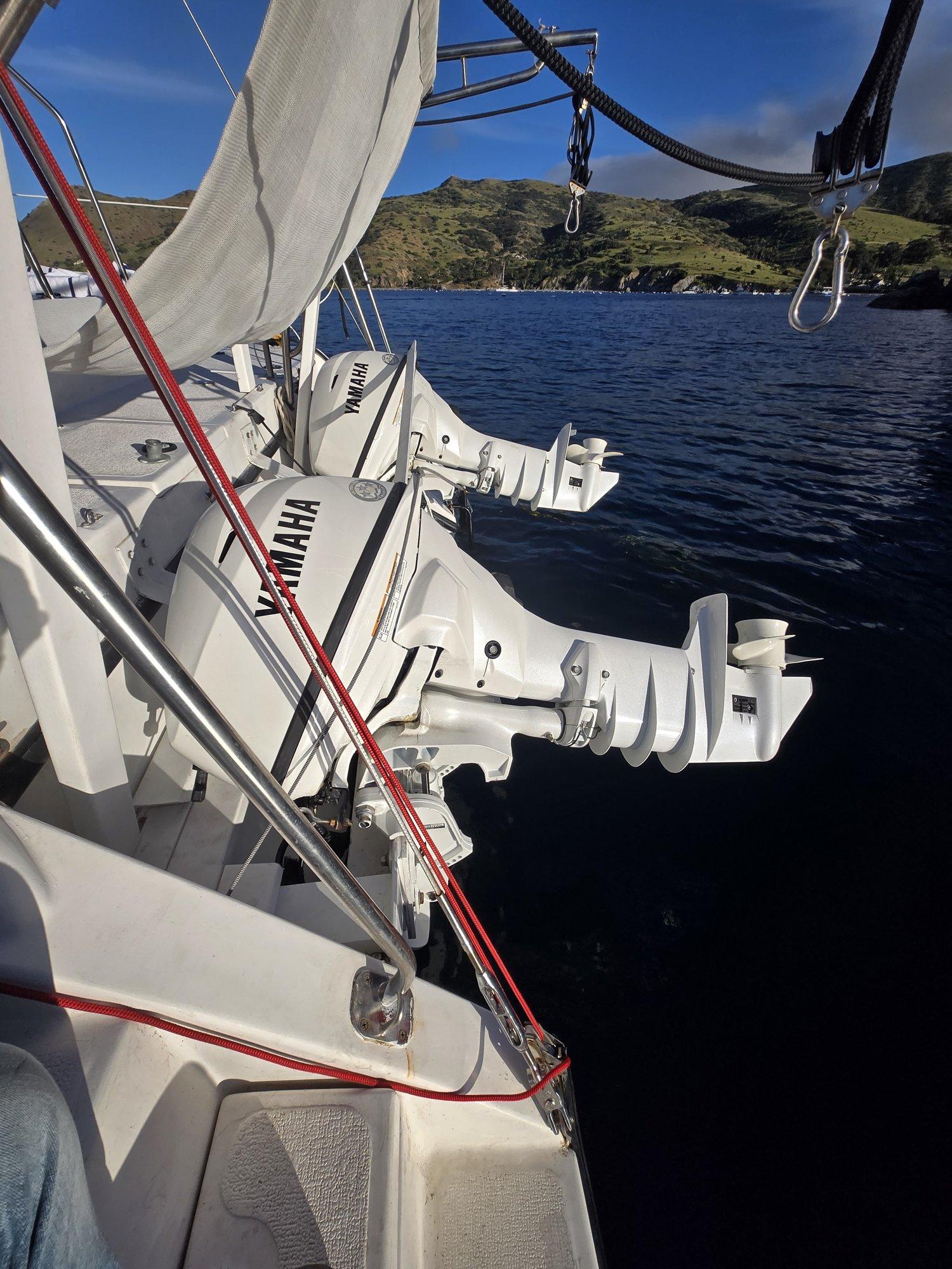 The twin white Yamaha T25 high-thrust outboard engines mounted on the stern of the catamaran, tilted up out of the water, with the hills of Catalina Island and calm blue water in the background.